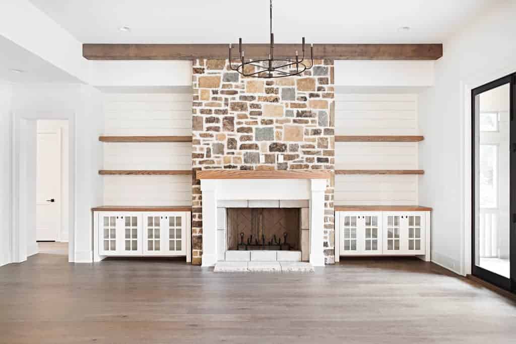 living room with stone fireplace and rustic beams featuring wide plank hardwood floors by Textures Nashville.