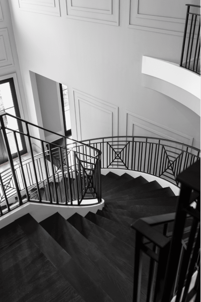 Elegant interior stairway with contrasting black and white tones, featuring ornate metal balustrades and geometric patterns on a herringbone wood floor.